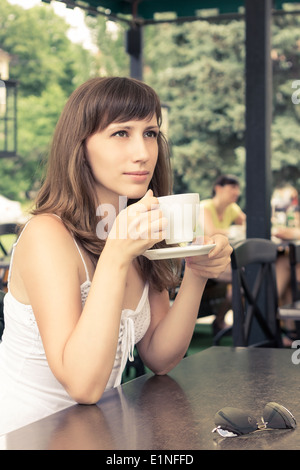 Portrait of young woman sitting in cafe. Fille de rêve avec une tasse de café. Les tons de couleurs chaudes de droit Banque D'Images