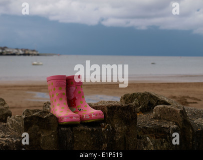 Paire de bottes pour enfants rose sur un mur à la plage, Instow, Devon, UK Banque D'Images