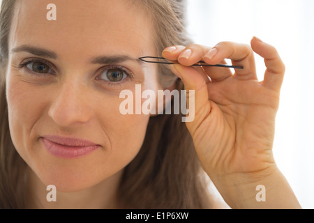 Portrait of happy young woman tweezing eyebrows Banque D'Images