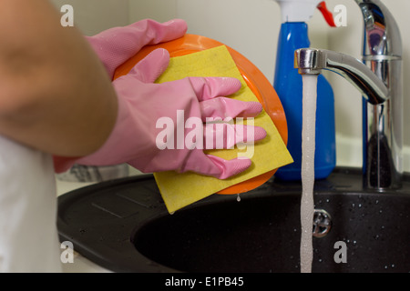 Femme faisant la vaisselle dans l'évier rincer une plaque sous l'eau courante avec un tissu plat Banque D'Images