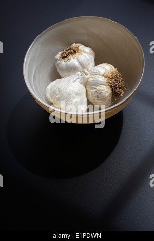 Trois bulbes d'ail s'asseoir dans un bol en verre blanc laiteux sur une table. Banque D'Images