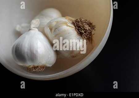 Trois bulbes d'ail s'asseoir dans un bol en verre blanc laiteux sur une table. Banque D'Images