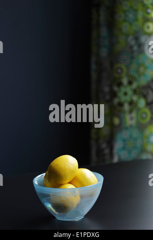 Les citrons dans un bol en verre bleu assis sur une table. Banque D'Images