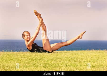 Jeune femme exerçant sur l'herbe par ocean Banque D'Images