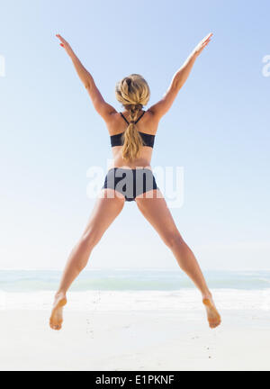 Blonde fit jumping on the beach with arms outstretched Banque D'Images