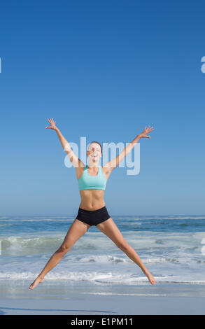 Fit woman jumping on the beach with arms out Banque D'Images
