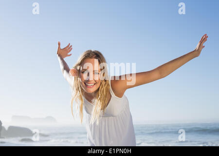 Jolie blonde souriant à la plage en robe blanche Banque D'Images