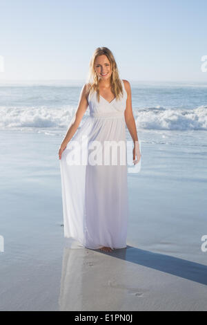Jolie blonde smiling at camera à la plage en robe blanche Banque D'Images