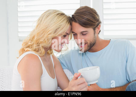 Smiling casual couple sitting on couch having coffee Banque D'Images