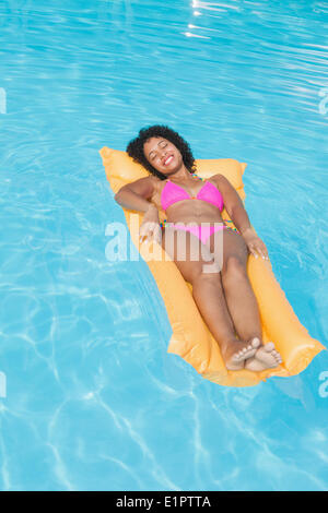 Smiling woman in pink bikini lying on lilo dans la piscine Banque D'Images