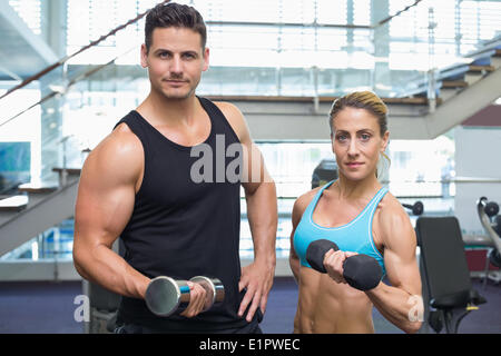 Bodybuilding man and woman holding dumbbells smiling at camera Banque D'Images