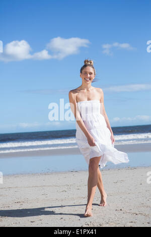 Blonde en robe blanche la marche sur la plage smiling at camera Banque D'Images