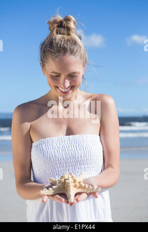 Jolie blonde en robe blanche holding starfish sur la plage Banque D'Images