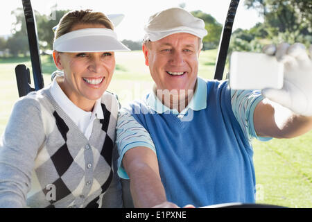 Heureux couple sitting in golf voiturette de golf en tenant un selfies Banque D'Images