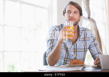 Bel homme de boire le jus d'orange au petit déjeuner Banque D'Images