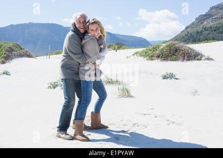 Smiling couple hugging sur la plage dans des vêtements chauds Banque D'Images