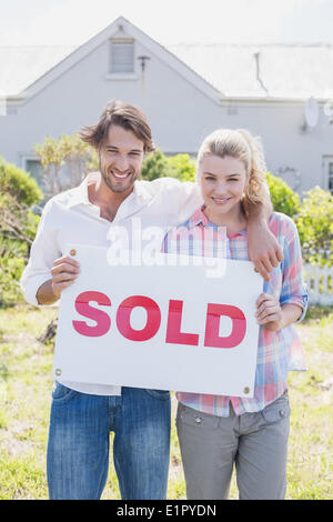 Heureux couple smiling at camera holding sold sign Banque D'Images