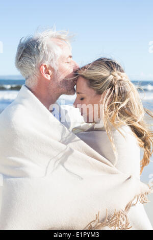 Affectionate couple enveloppé dans la couverture sur la plage Banque D'Images