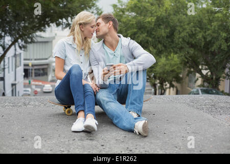 Hip young couple sitting on skateboard kissing Banque D'Images