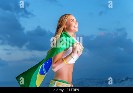 Heureux fan de l'équipe de football brésilienne, cheerful pretty girl on stadium à l'appui, d'encouragement holding big drapeau national du Brésil Banque D'Images