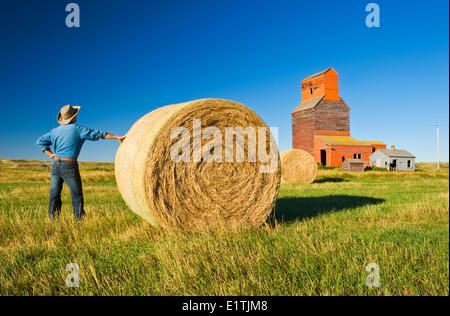 Un agriculteur se face au vieux silos à grain et des balles de foin rondes , ville fantôme de Neidpath, Saskatchewan, Canada Banque D'Images