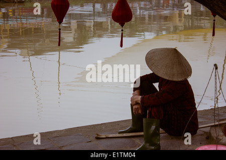 L'homme à l'échelle du vietnamien la rivière Thu Bon à Hoi An, au Vietnam, les bâtiments reflètent dans l'eau. Banque D'Images