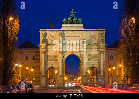 La Siegestor (Porte de la Victoire) avec trafic circulant autour d'elle à la tombée de la nuit dans le quartier de Schwabing dans la Ville München (Munich) Banque D'Images