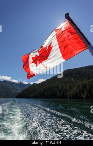 Le drapeau canadien vole de la poupe du Uchuck 111 tandis qu'elle traverse Esperanza Inlet, en Colombie-Britannique, Canada. Banque D'Images