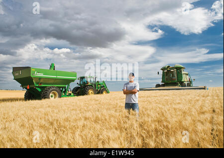 Jeune agriculteur dans son champ de blé dur à maturité au cours de la Moisson de céréales moissonneuse-batteuse de chariot dans le fond près de Ponteix en Saskatchewan Banque D'Images