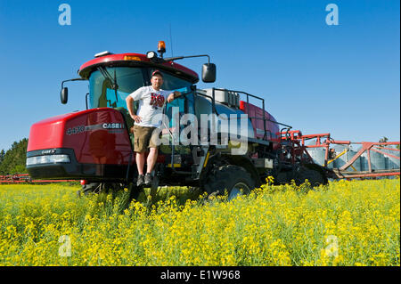 Agriculteur sur pulvérisateur enjambeur dans champ de canola près de Dugald (Manitoba), Canada Banque D'Images