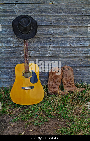 Acoutic guitare, chapeau de cowboy, bottes de cowboy et ancienne ferme de paroi de l'habitacle. Les régions rurales de l'Alberta, Canada. Banque D'Images