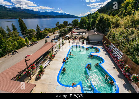 Salon des gens dans la piscine à Ainsworth Hot Springs Resort, avec le lac Kootenay à l'arrière-plan. Banque D'Images