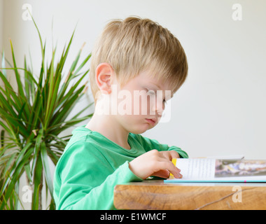 Un petit garçon la lecture d'un livre à une table Banque D'Images