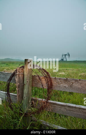 Barbelés sur piquet avec pumpjack en arrière-plan, au crépuscule, en Alberta, Canada Banque D'Images