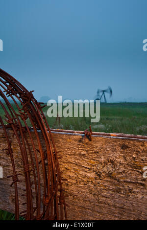 Barbelés sur piquet avec pumpjack en arrière-plan, au crépuscule, en Alberta, Canada Banque D'Images