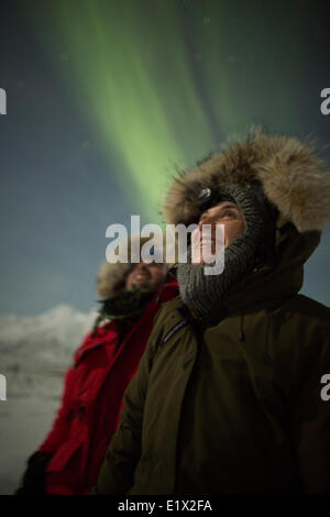 Les gens sourire en regardant les aurores boréales danser dans le ciel nocturne au-dessus d'eux, au Yukon. Banque D'Images