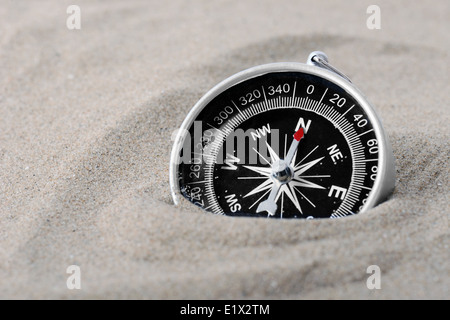 Une boussole partie enterrée dans le sable avec l'aiguille pointée vers le nord Banque D'Images