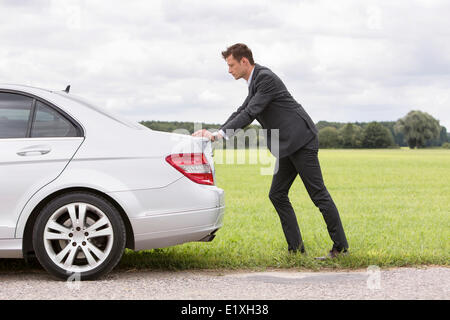 Full Length side view of young businessman pushing ventilées voiture à la campagne Banque D'Images