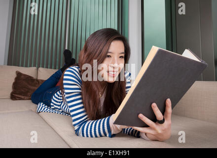 Young woman reading book détendue à la maison Banque D'Images