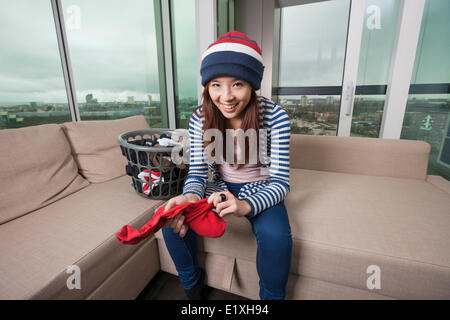 Portrait of smiling young woman doing laundry travailler dans la salle de séjour à la maison Banque D'Images