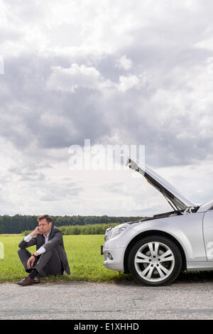 Toute la longueur du malheureux jeune homme assis ventilées par voiture à la campagne Banque D'Images