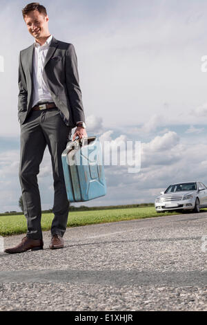 Toute la longueur du jeune homme transportant du gaz peut avec voiture décomposée en tâches de fond à campagne Banque D'Images