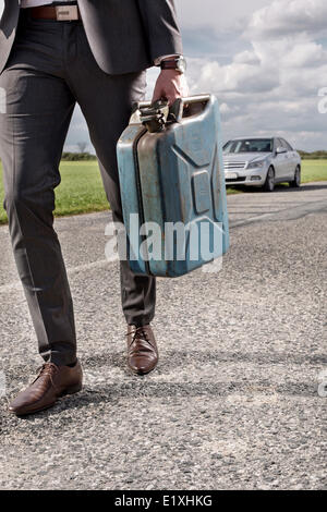 La section basse of young businessman transportant du gaz peut avec voiture cassée en arrière-plan à campagne Banque D'Images