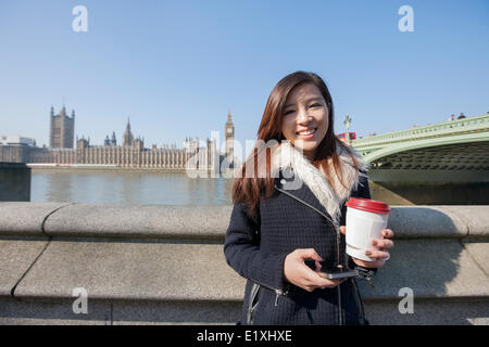 Portrait of happy young woman holding cell phone et gobelet jetable contre Big Ben à Londres, Angleterre, Royaume-Uni Banque D'Images