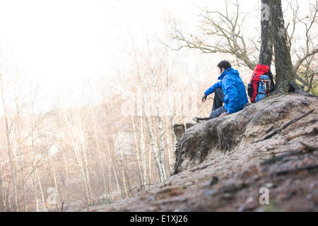 Vue latérale du male hiker assis sur le bord de la falaise en forêt Banque D'Images