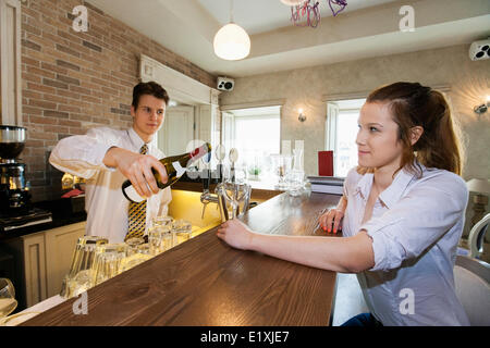 Bartender pouring wine for female customer at restaurant counter Banque D'Images