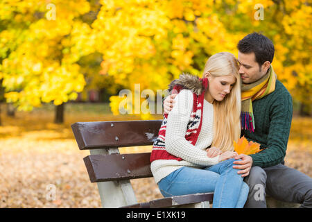 Jeune homme aimant hugging femme timide sur banc de parc au cours de l'automne Banque D'Images