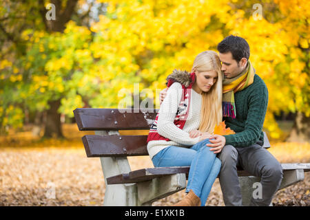 Jeune homme serrant femme timide sur banc de parc au cours de l'automne Banque D'Images