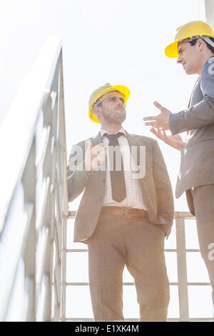 Low angle view of young male hommes d'avoir des casques de discussion sur l'escalier contre ciel clair Banque D'Images