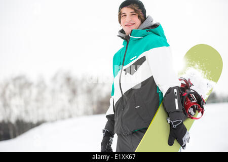 Portrait of handsome young man with snowboard dans la neige Banque D'Images